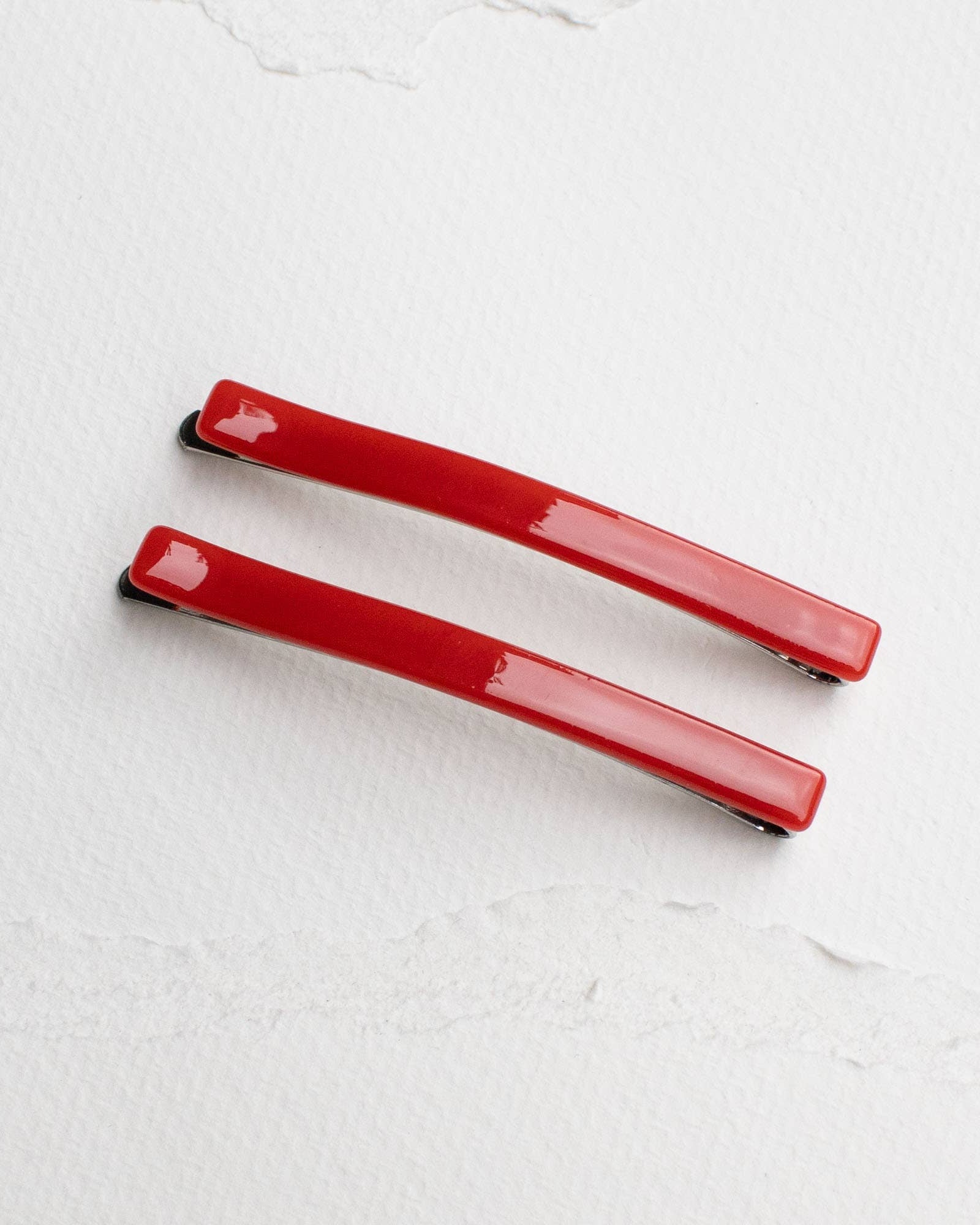 A set of two red bobby pins on a white background