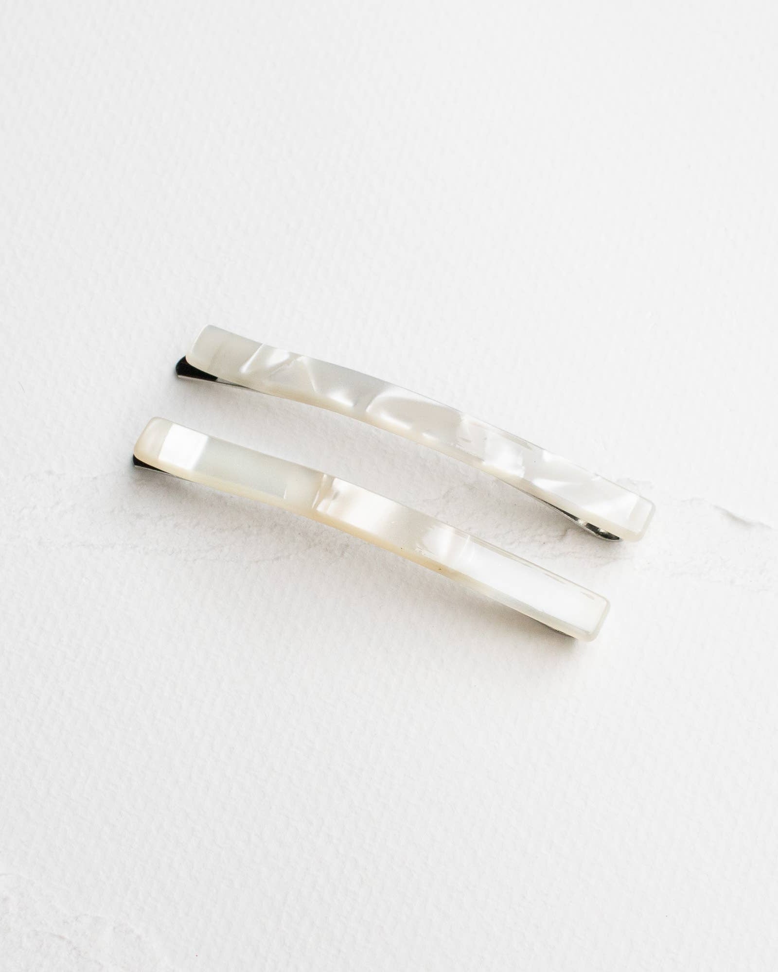 A pair of simple white bobby pins placed on a white surface.
