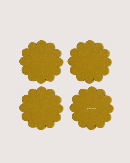 Four mustard yellow flower-shaped coasters on a light beige background